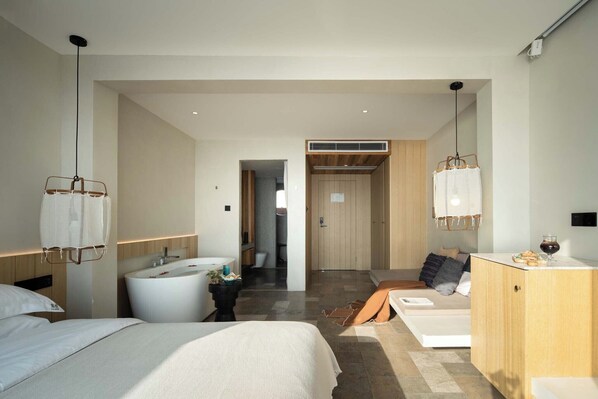 Egy modern szállodai szoba, amelyben egy nagy ágy, egy pihenősarok, fürdőkádas fürdőszoba és egy minibar található.