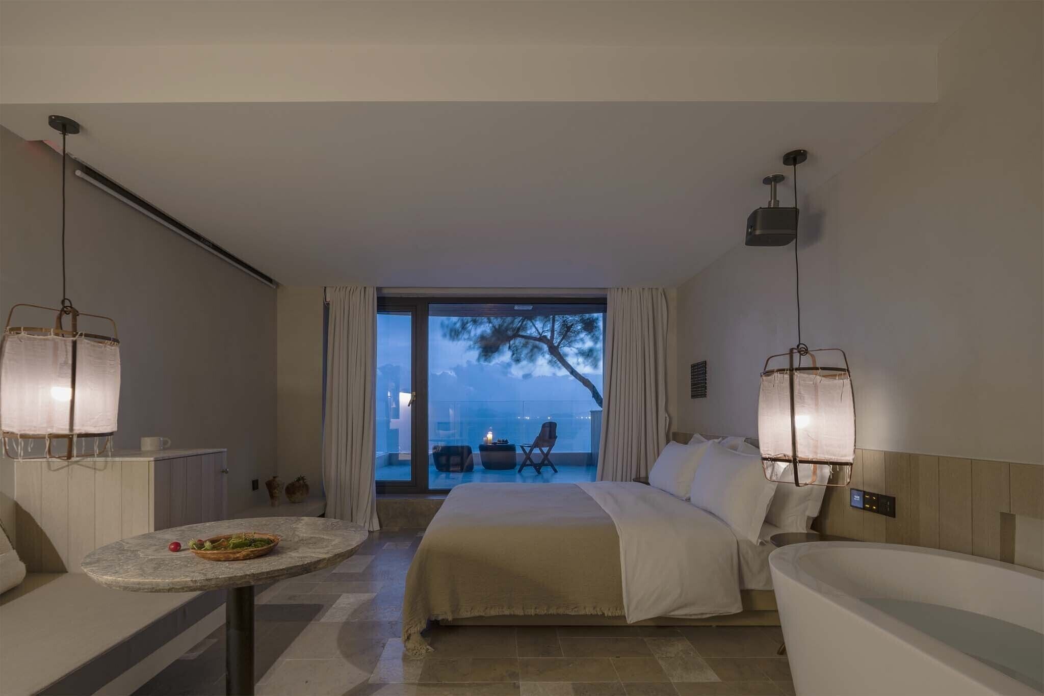 Habitación de hotel con cama, zona de estar con mesa y vistas al exterior.