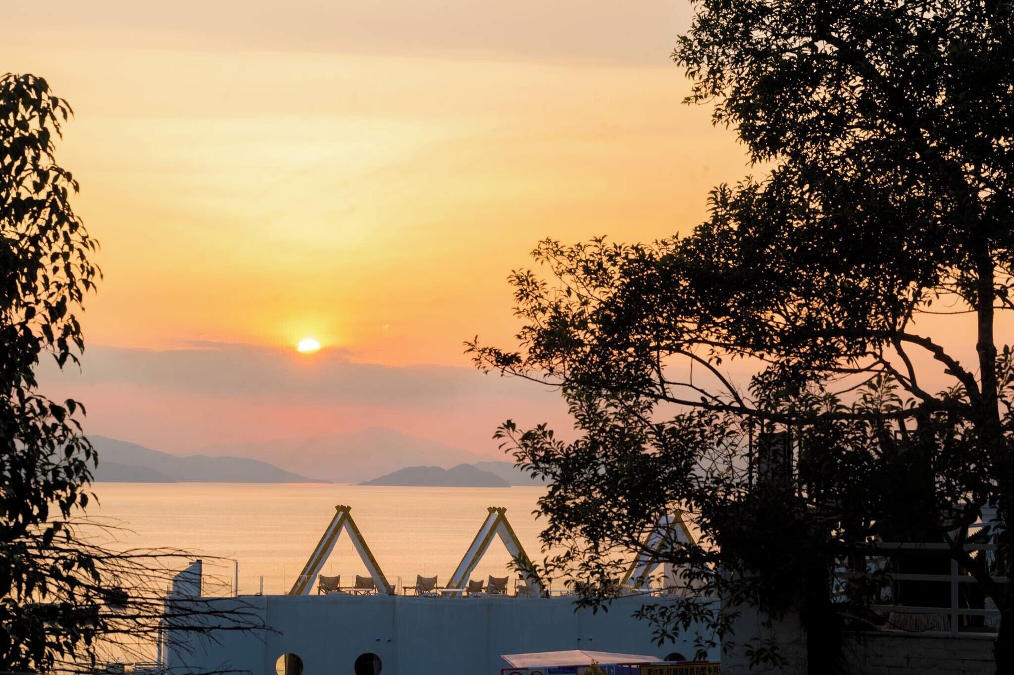 A sunset view over a calm sea with a beach area and a building with a white facade.