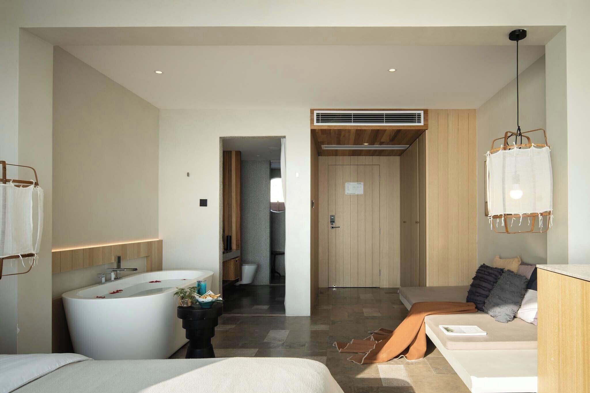 Una habitación de hotel moderna con una bañera grande, una zona de ducha separada, una puerta de madera y un colgante de luz.