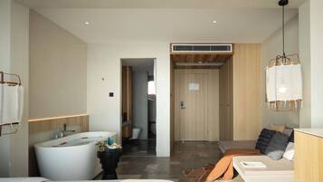 Una habitación de hotel moderna con una bañera grande, una zona de ducha separada, una puerta de madera y un colgante de luz.