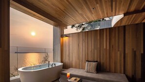 Un bagno moderno con una vasca da bagno freestanding, un'area salotto con un cuscino e vista sull'acqua.