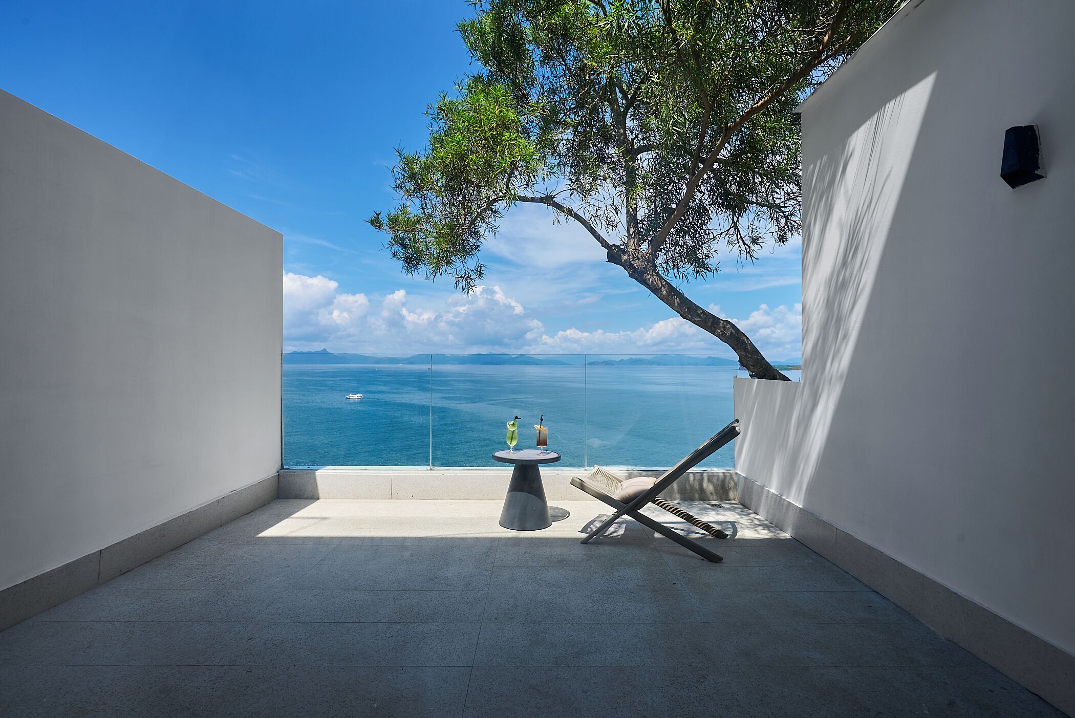 Un balcon avec vue sur la mer, une table avec des boissons et un fauteuil de relaxation.