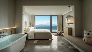 Una camera d'albergo moderna con una vasca da bagno grande, un letto con vista sul mare e un'area salotto con vista.