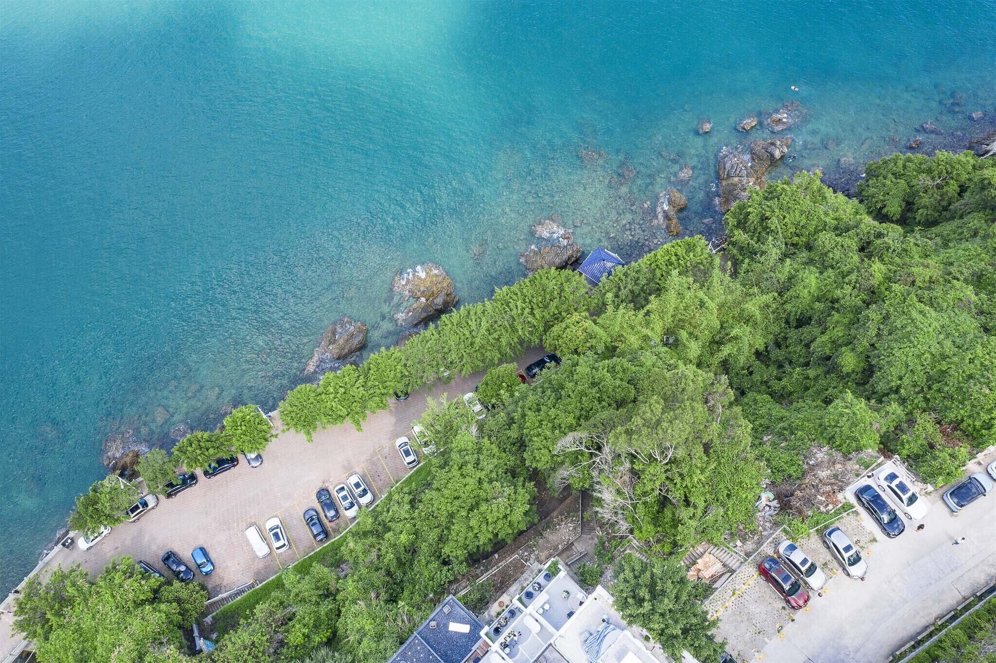 An aerial view of a coastal area with a parking lot, a beach, and rocky outcrops.