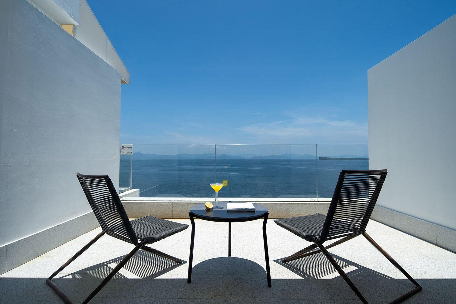 Un balcon avec deux chaises noires et une petite table, offrant une vue panoramique sur la mer.