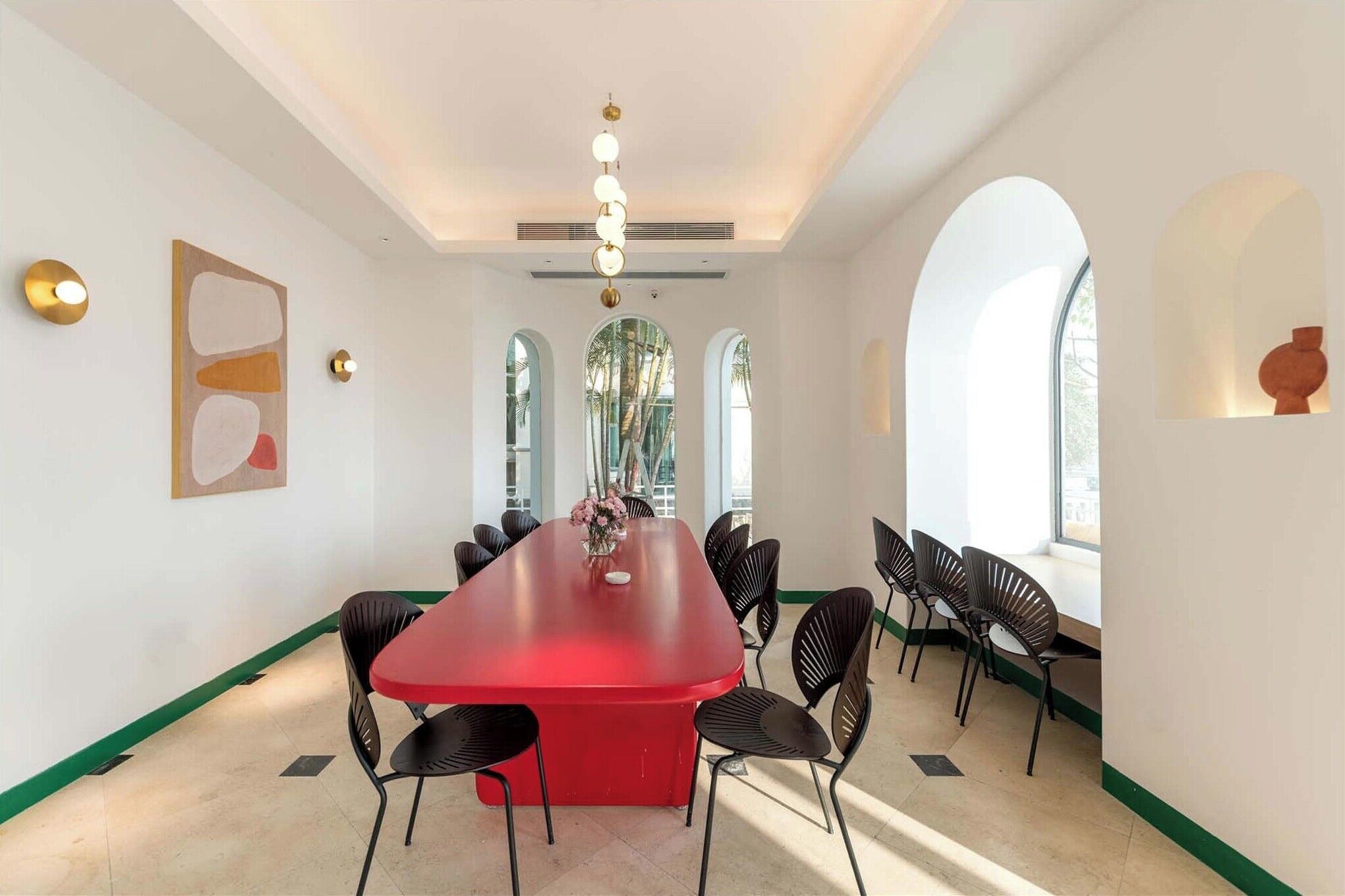 A conference room with a red table, black chairs, and a modern chandelier.