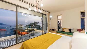 Een moderne hotelkamer met een groot bed, een bank, een fauteuil en uitzicht op de skyline door raam-tot-plafond ramen.