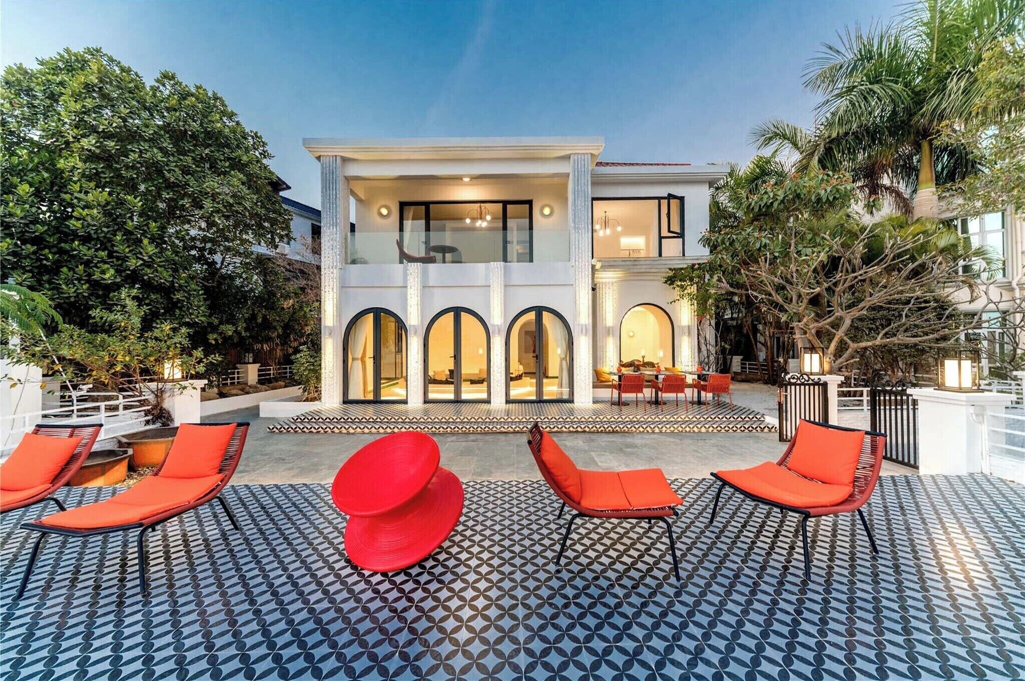 A modern house with a pool area featuring red lounge chairs and patterned flooring.