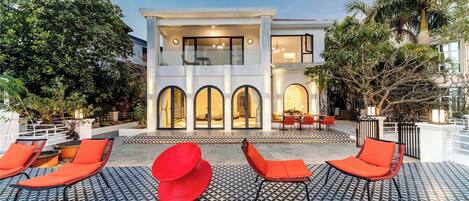 A modern house with a pool area featuring red lounge chairs and patterned flooring.