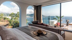 Habitación de hotel moderna con una cama grande, vista al mar y un balcón con bañera y zona de estar.