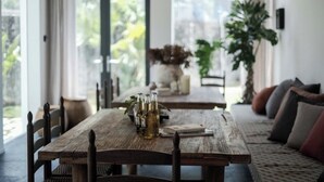 Un comedor con una mesa de madera dispuesta para dos personas, un jarrón con flores y vistas a la vegetación exterior.