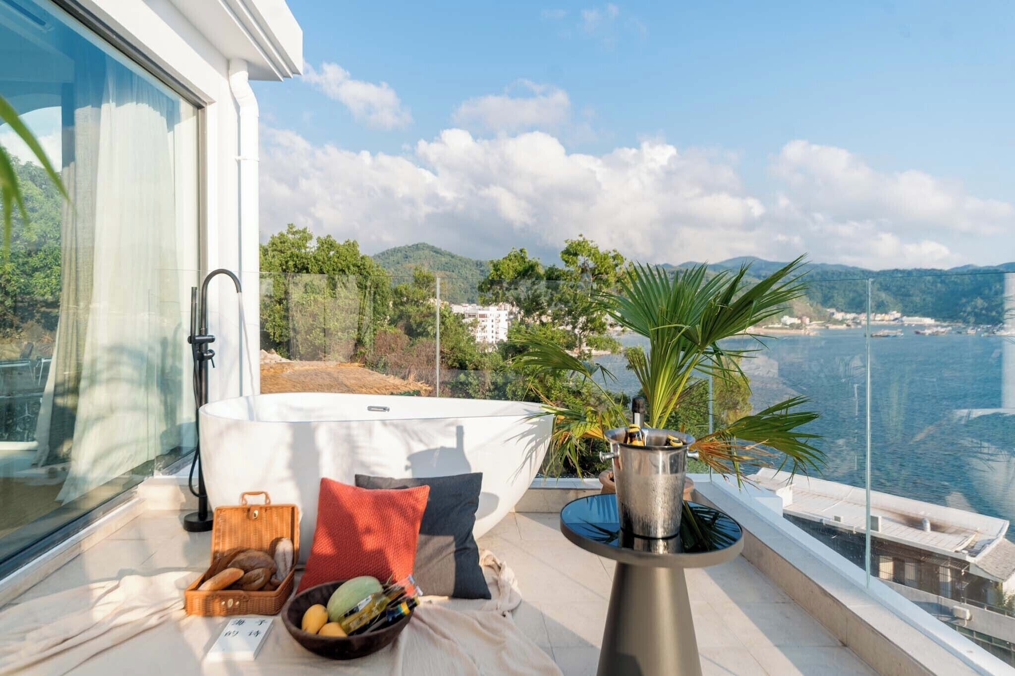 A balcony with a view of the sea, a table with a bottle, and a basket of bread.
