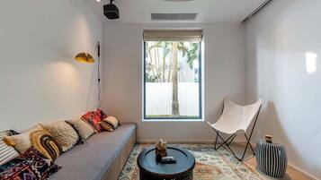 Una sala de estar moderna con un sofá, un sillón, una mesita y una ventana con vistas a palmeras.
