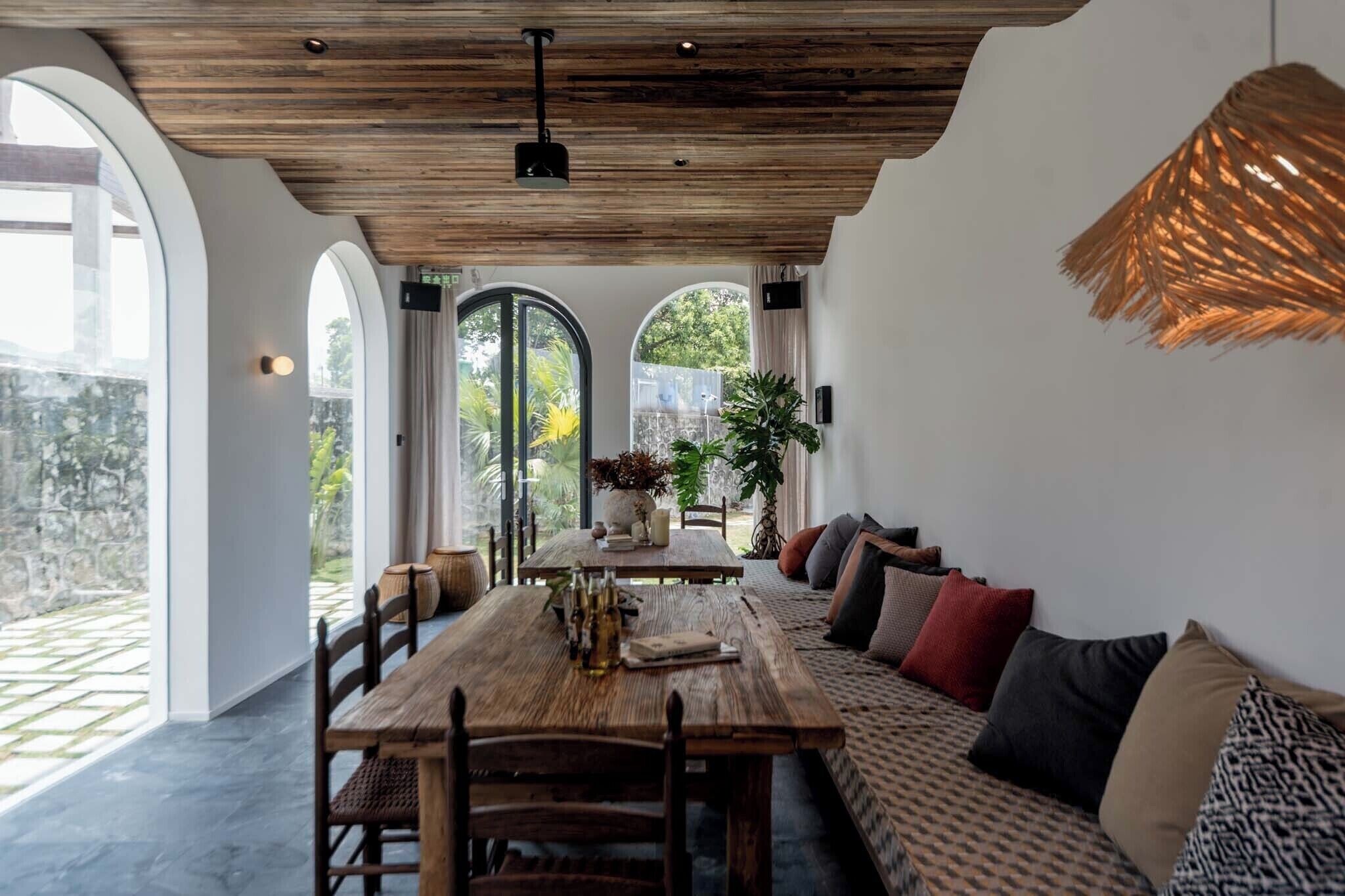 A dining area with a wooden table and chairs, a sofa with cushions, and a hanging light fixture.
