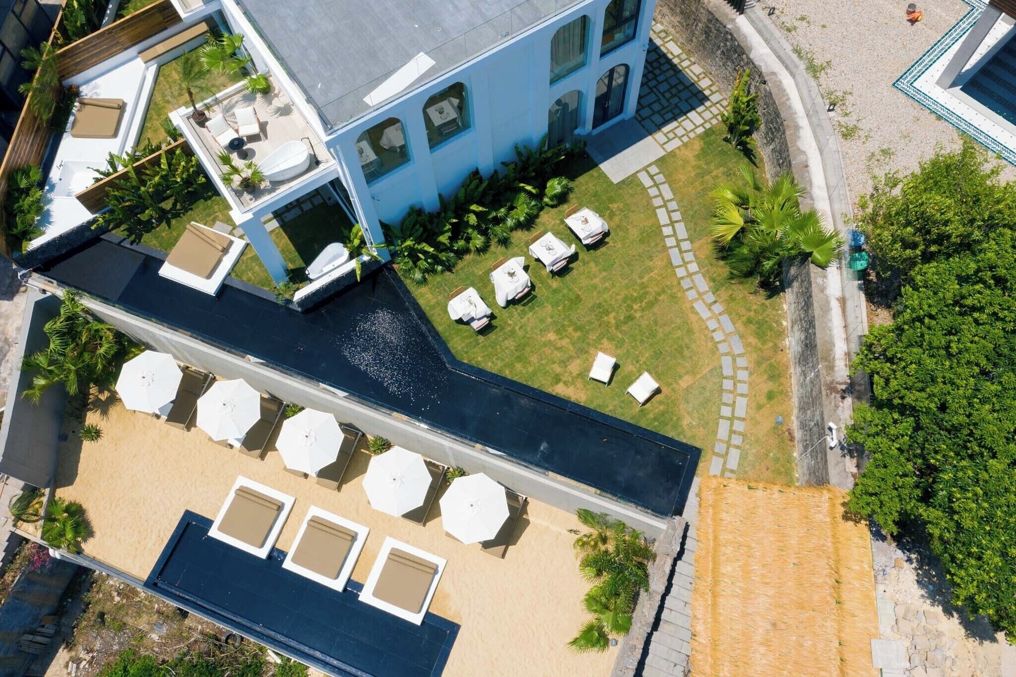 Vista aérea de un hotel con piscina en la azotea, zona de estar al aire libre y césped cuidado.