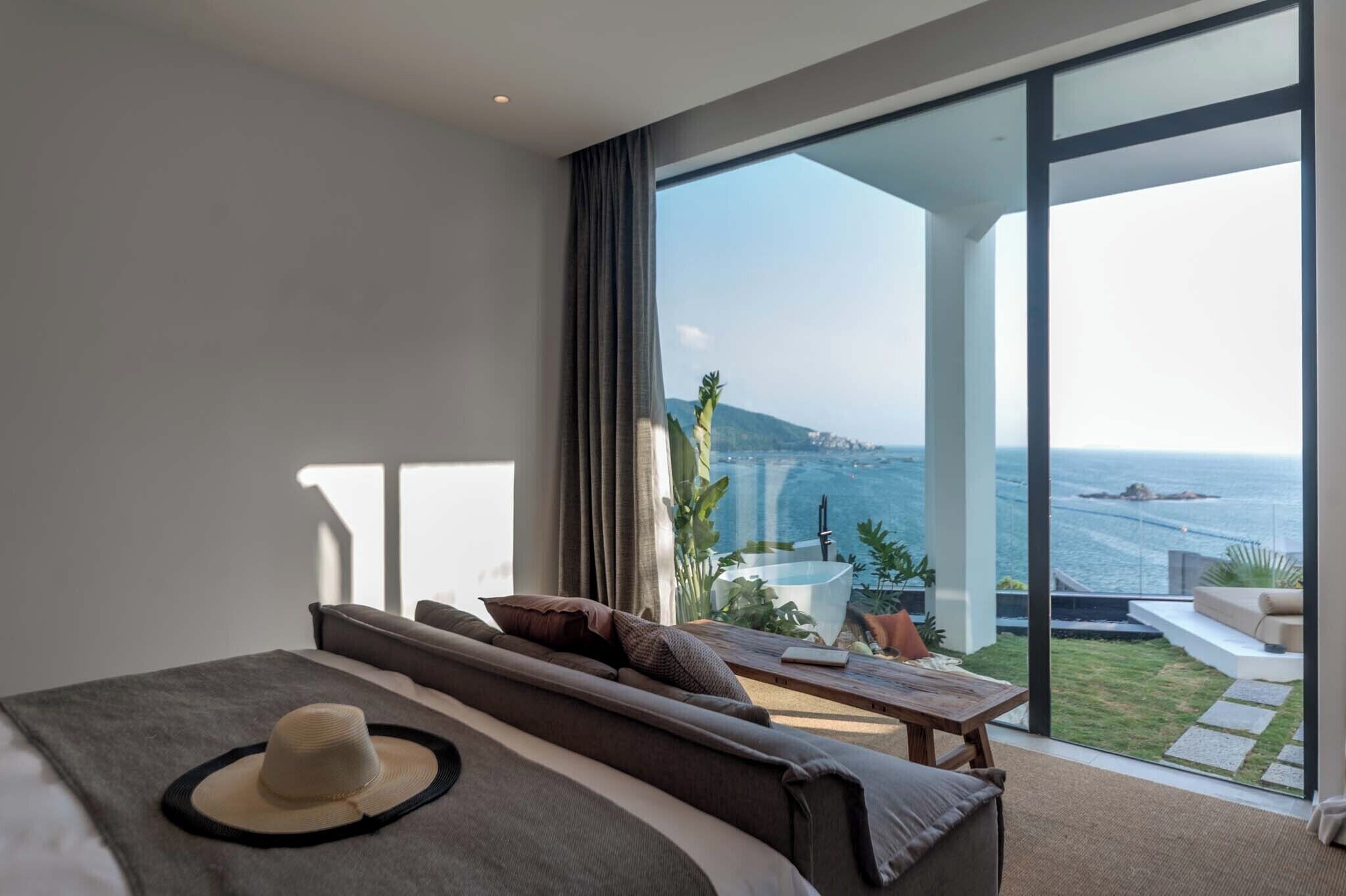 A modern bedroom with a large bed, a view of the sea, and a balcony with outdoor seating.