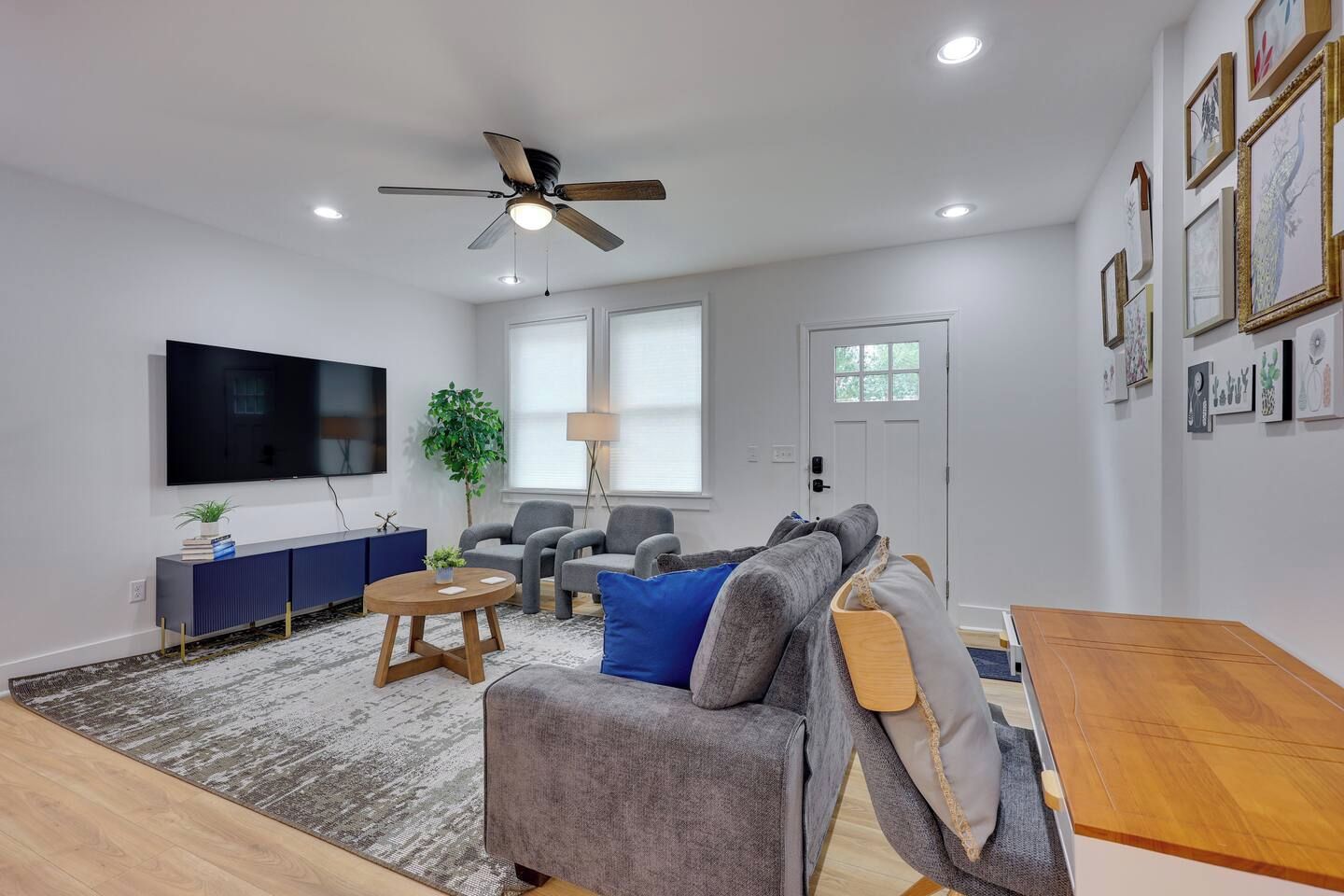 A modern living room with a flat-screen TV, grey sofas, a wooden coffee table, and a ceiling fan.