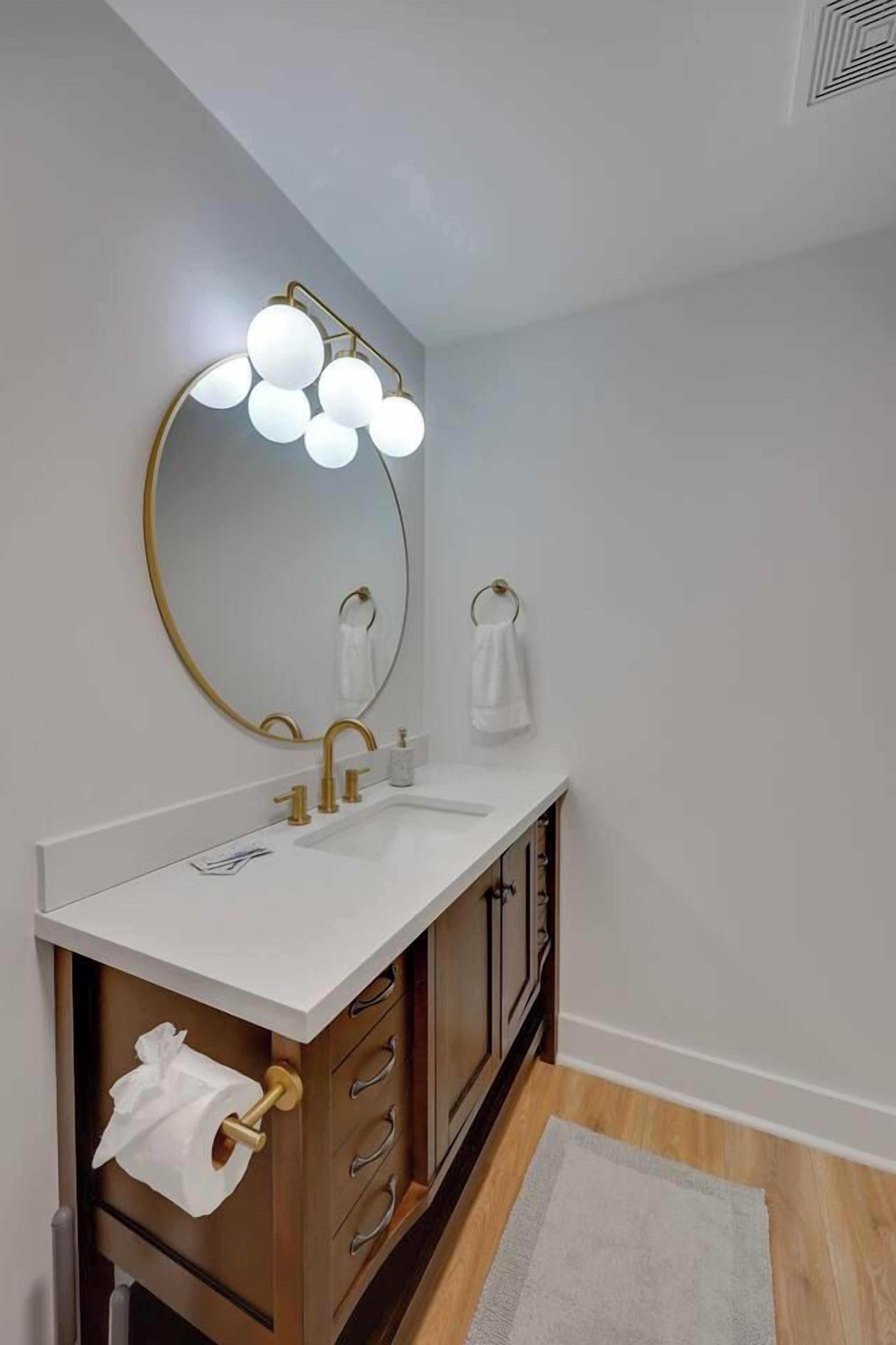 A bathroom with a round mirror, gold faucets, a white sink, and a towel rack.