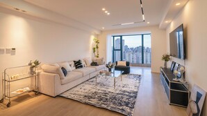 Un salon moderne avec une grande fenêtre, un canapé, une table basse et un téléviseur fixé au mur.