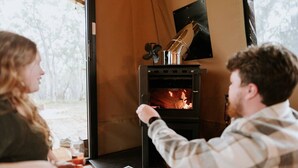 Une pièce chaleureuse avec une cheminée, une fenêtre et une table sur laquelle se trouvent un magazine et un verre de vin.