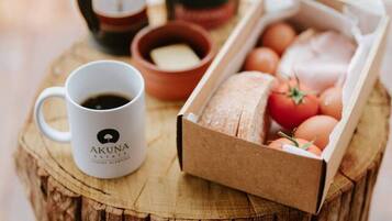 A rustic wooden table with a coffee pot, a mug labeled "AKUNA," a small bowl, and a cardboard box containing eggs and tomatoes.
