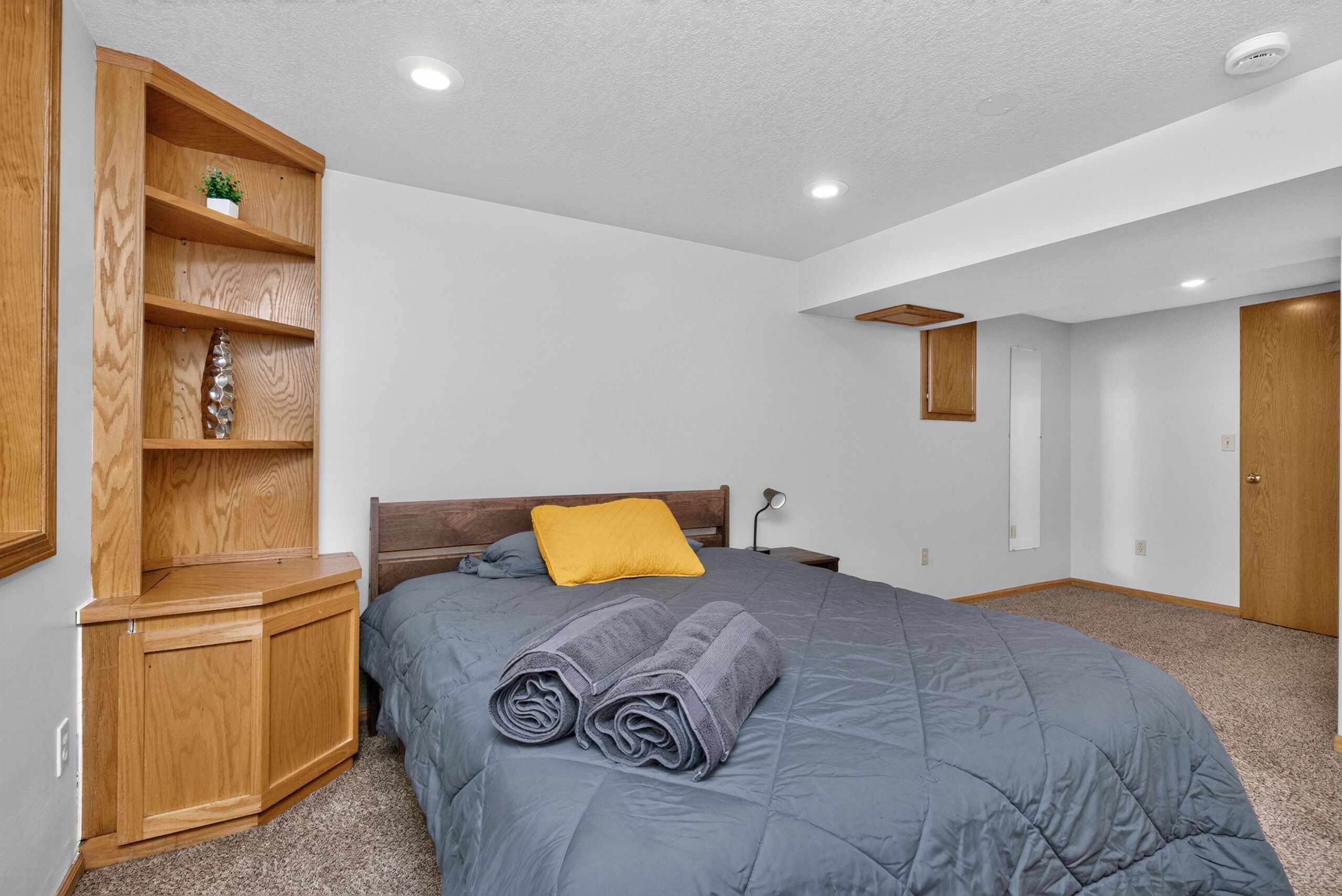 A bedroom with a bed, a wooden wardrobe, a bedside table, and a small shelf with a plant.