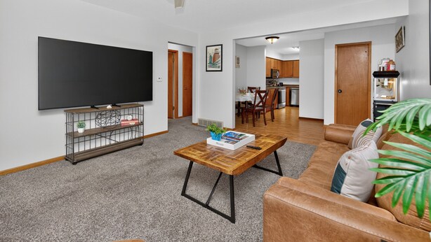 Ein Wohnzimmer mit Flachbildfernseher, Couchtisch, Sofa, Deckenventilator und einer Küche im Hintergrund.