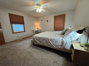 A bedroom with a bed, a desk, a chair, a ceiling fan, and a window.