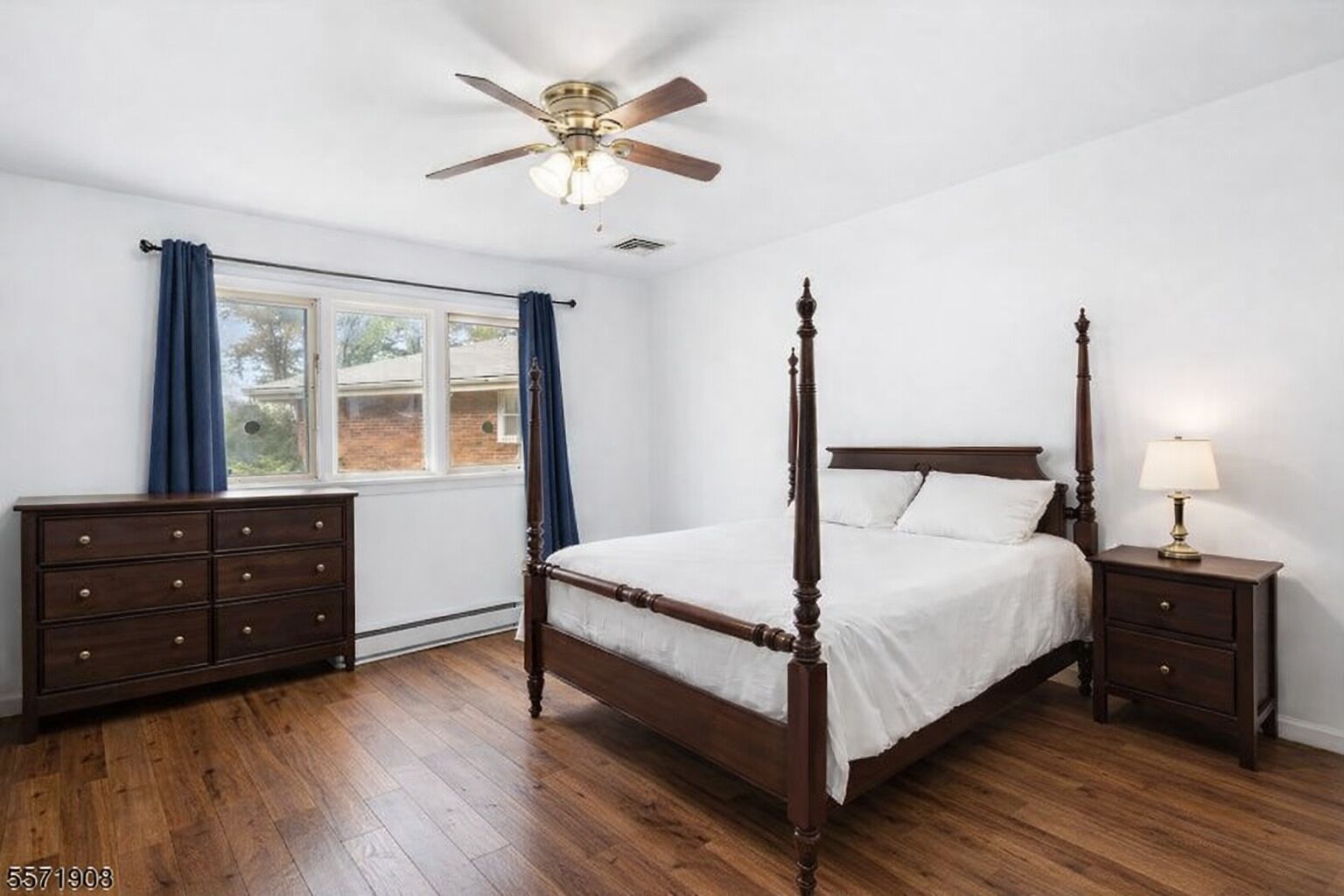 A bedroom with a four-poster bed, a dresser, a nightstand with a lamp, a ceiling fan, and a window with curtains.