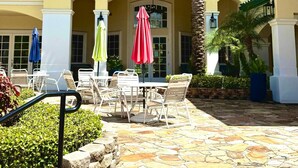 A courtyard with outdoor seating, palm trees, and a building with a green roof and columns. - Wonderful apartment 10 minutes from Disney (Kissimmee)
