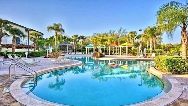 A circular pool with clear blue water, surrounded by lounge chairs and palm trees. - Wonderful apartment 10 minutes from Disney (Kissimmee)