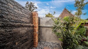 A stone wall with a metal gate, a concrete wall, and a tiled roof structure in the background.