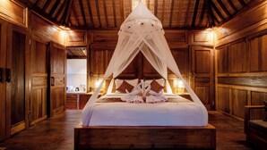 A large wooden room with a bed under a canopy, wooden walls, and a visible kitchen area.
