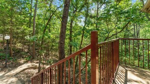 A wooden deck with a metal railing overlooking a forested area.
