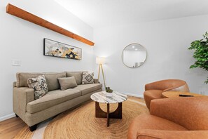 A modern living room with a sofa, a round table, a lamp, a mirror, and a plant. - Updated Bungalow_Huge Outdoor Deck_Outdoor Pool Open & Resort Lake Access_Mini Golf_Free Tickets! (Kimberling City)