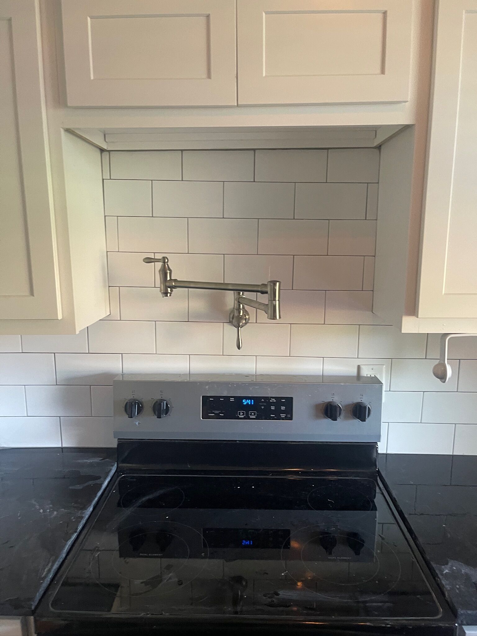 A kitchen with white cabinets, a stainless steel range hood, and a black oven.