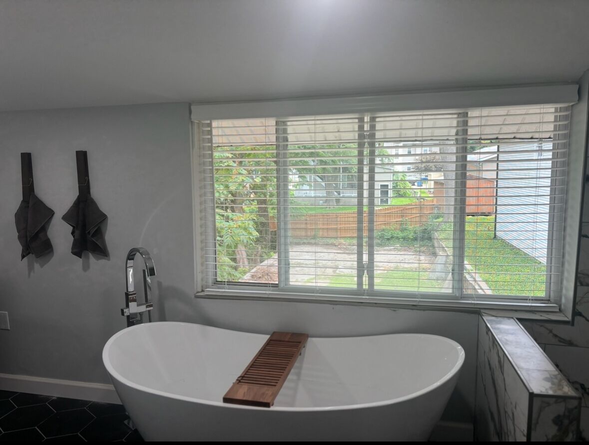A bathroom with a freestanding bathtub, a window with blinds, and a towel rack.