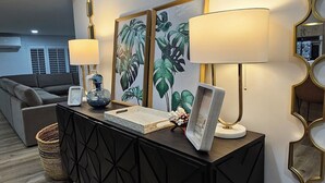 Ein modernes Wohnzimmer mit einem dunklen Holzkonsole, zwei Lampen, gerahmten Kunstwerken und einem dekorativen Spiegel.