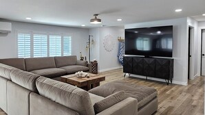 Ein geräumiges Wohnzimmer mit einem großen Ecksofa, einem Flachbildfernseher und einem Holztisch.