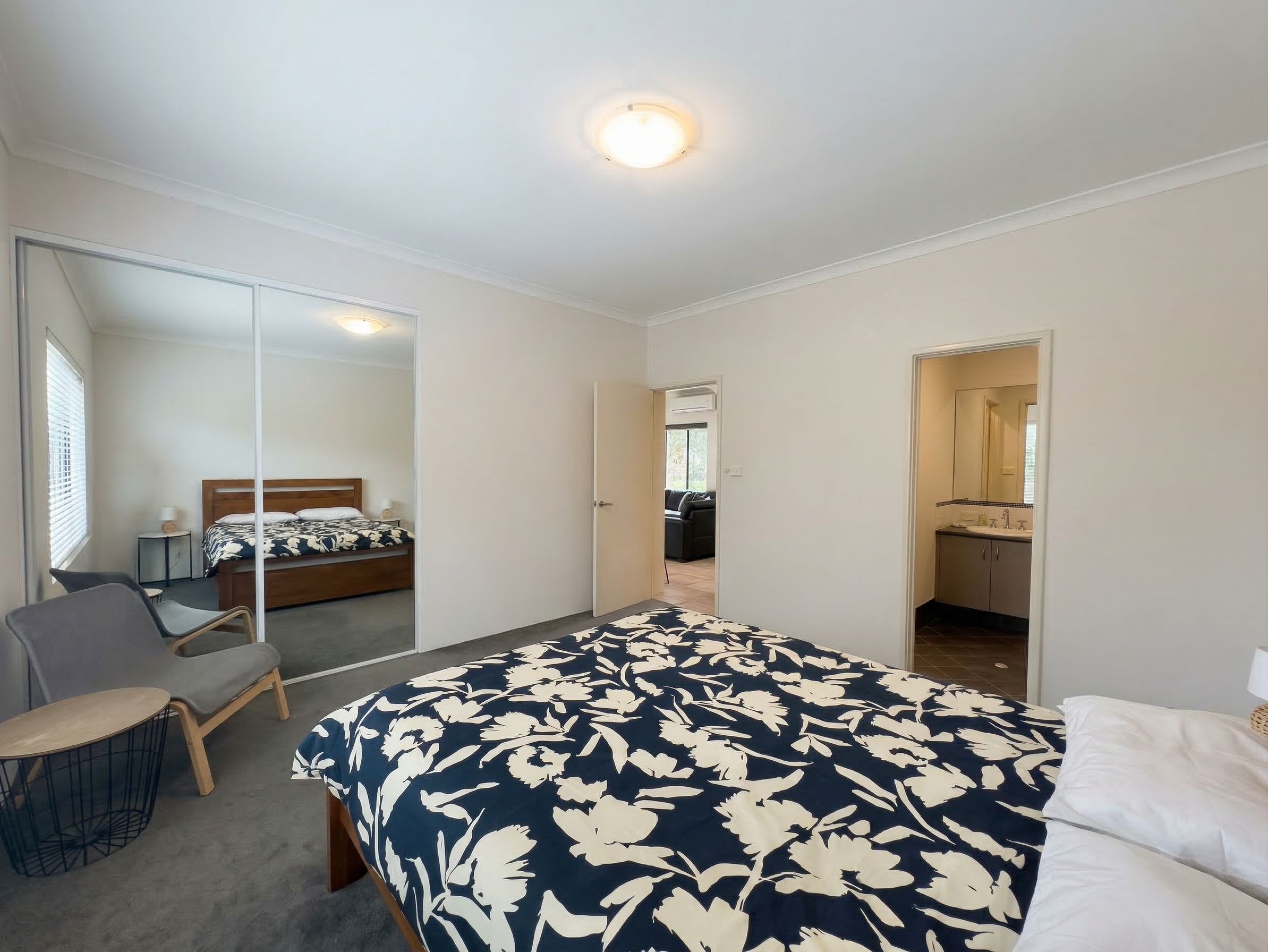 A bedroom with a bed, a chair, a mirror, and a bathroom visible through an open door.