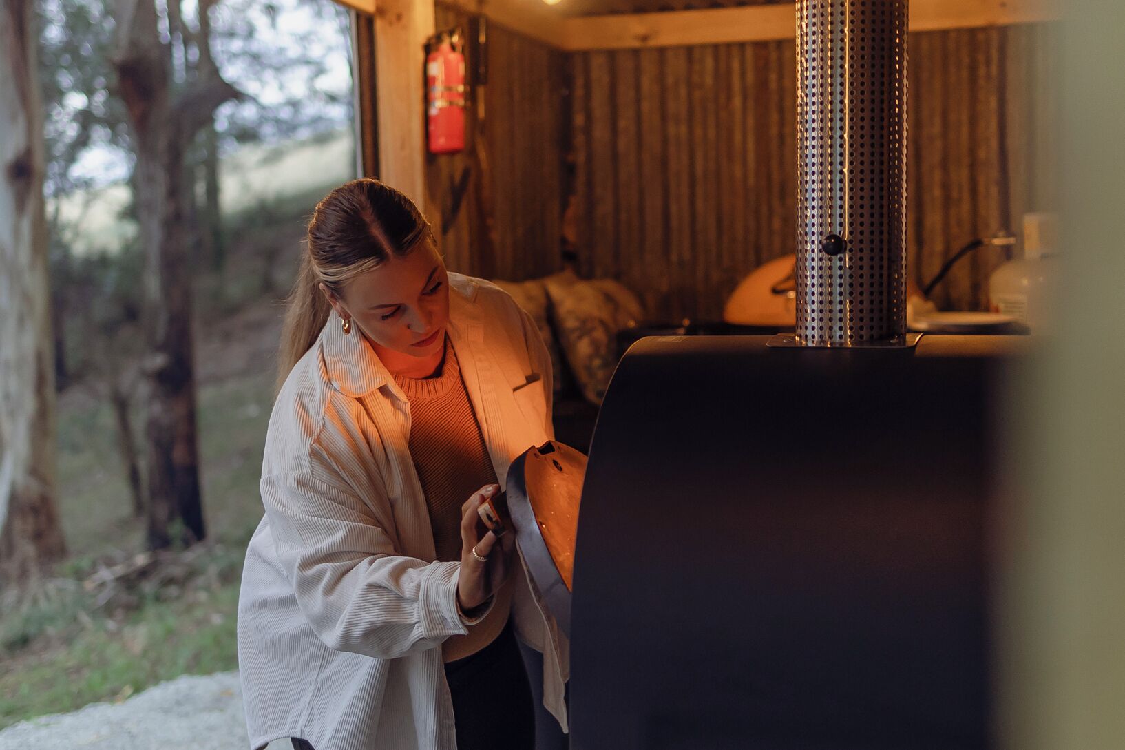 A person adjusting a grill in a rustic cabin with wooden walls and a fire extinguisher on the wall.