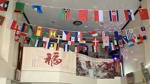 Un hall d’hôtel avec de nombreuses tables et chaises, un comptoir d’accueil et une grande banderole décorative ornée de drapeaux.