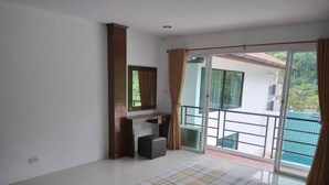 A bedroom with a bed, a desk, a chair, a mirror, and a balcony with a view of the outside.