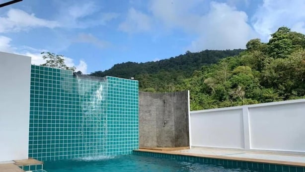 A swimming pool with a tiled wall and a view of a forested hill.