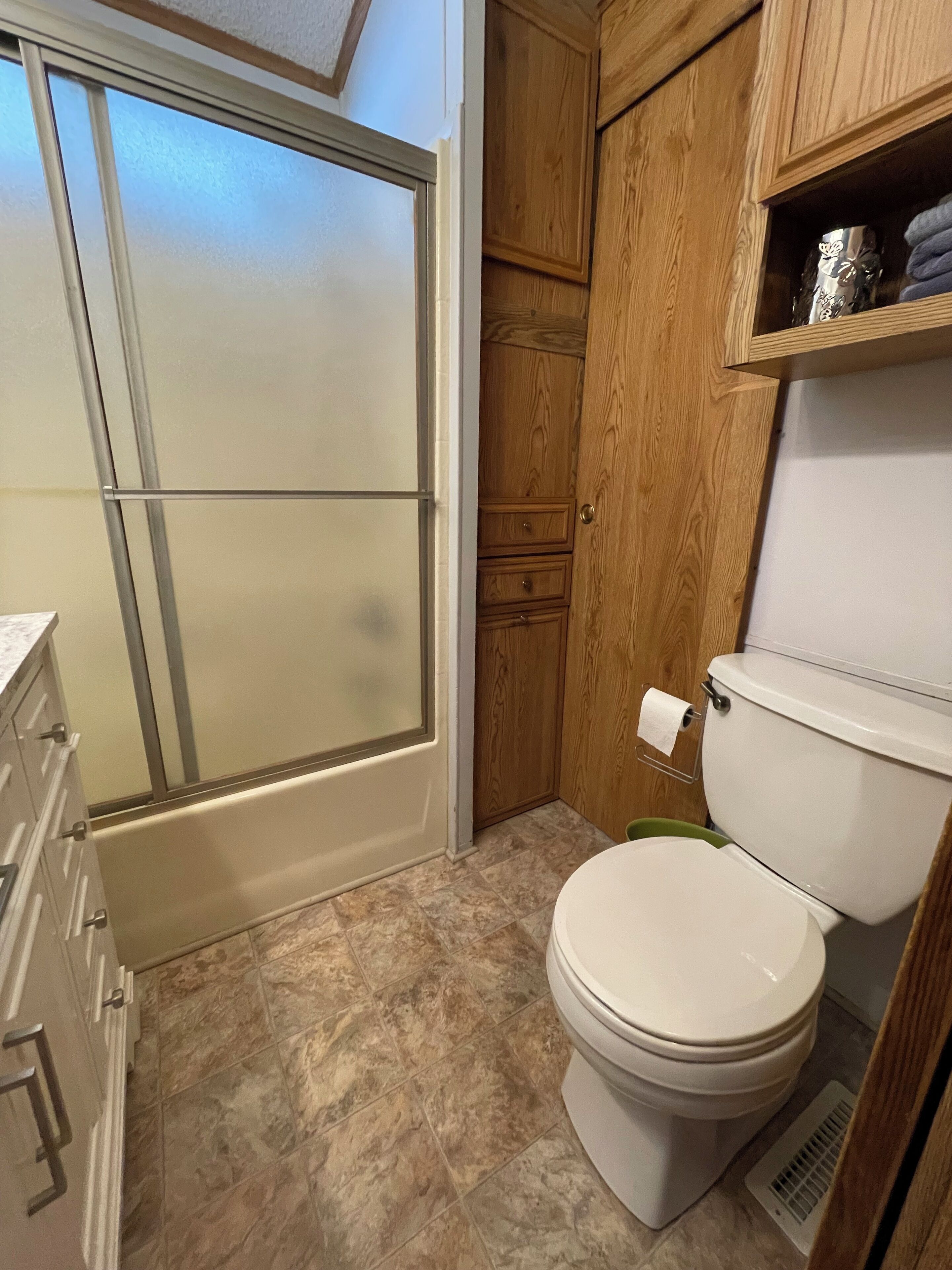A bathroom with a toilet, a shower, and wooden cabinets.