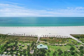 An aerial view of a beach resort with a long stretch of beach, palm trees, and a central building. - Stunning Marco Condo l Million-Dollar Views! (Marco Island)