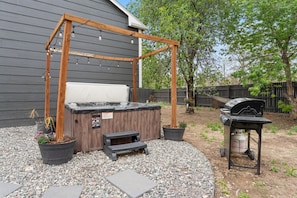 Un bain à remous agrémenté d’une pergola en bois, un barbecue et des plantes en pot dans un jardin.