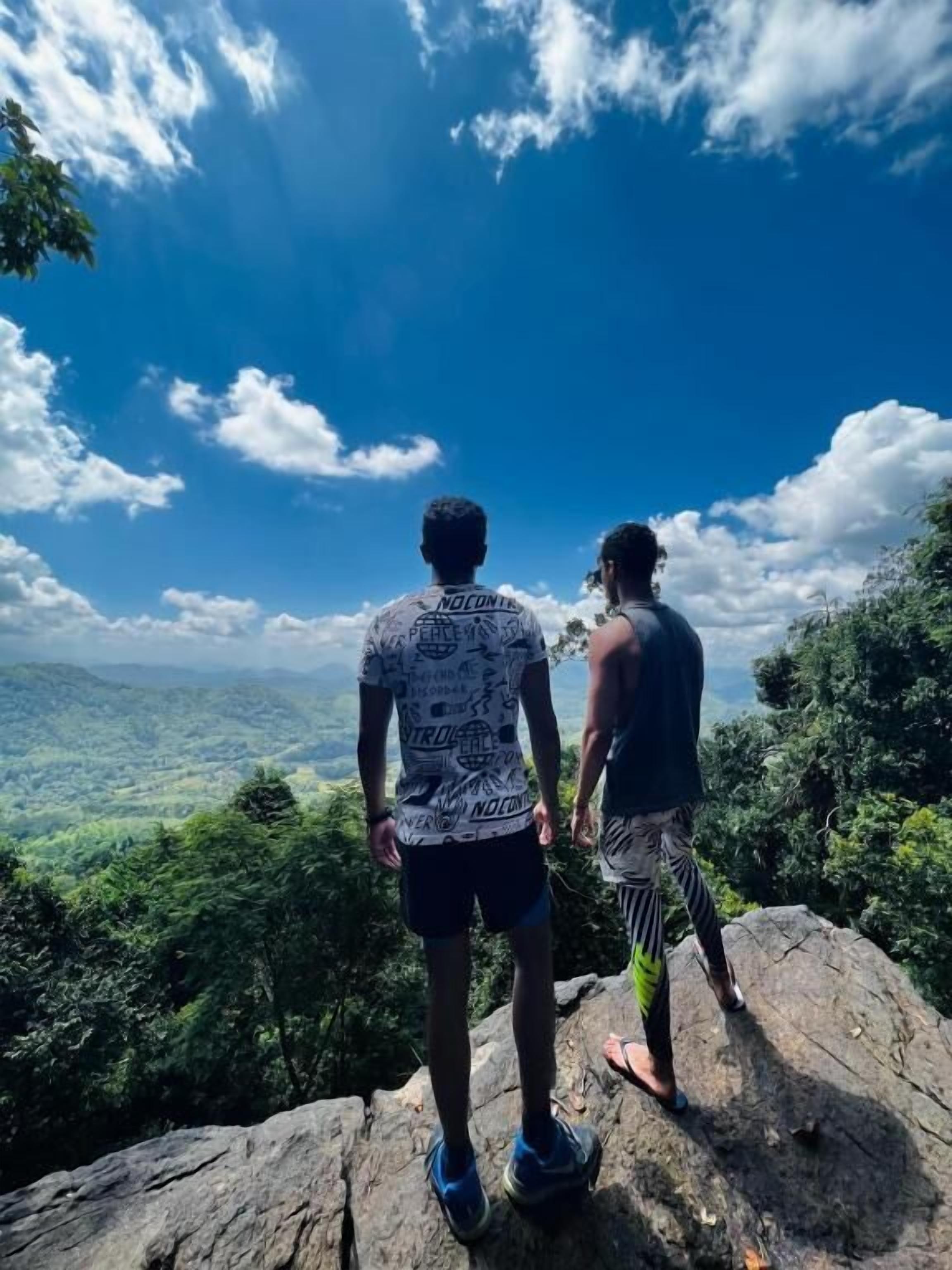 Dos personas de pie sobre un afloramiento rocoso, con vistas a un valle exuberante.
