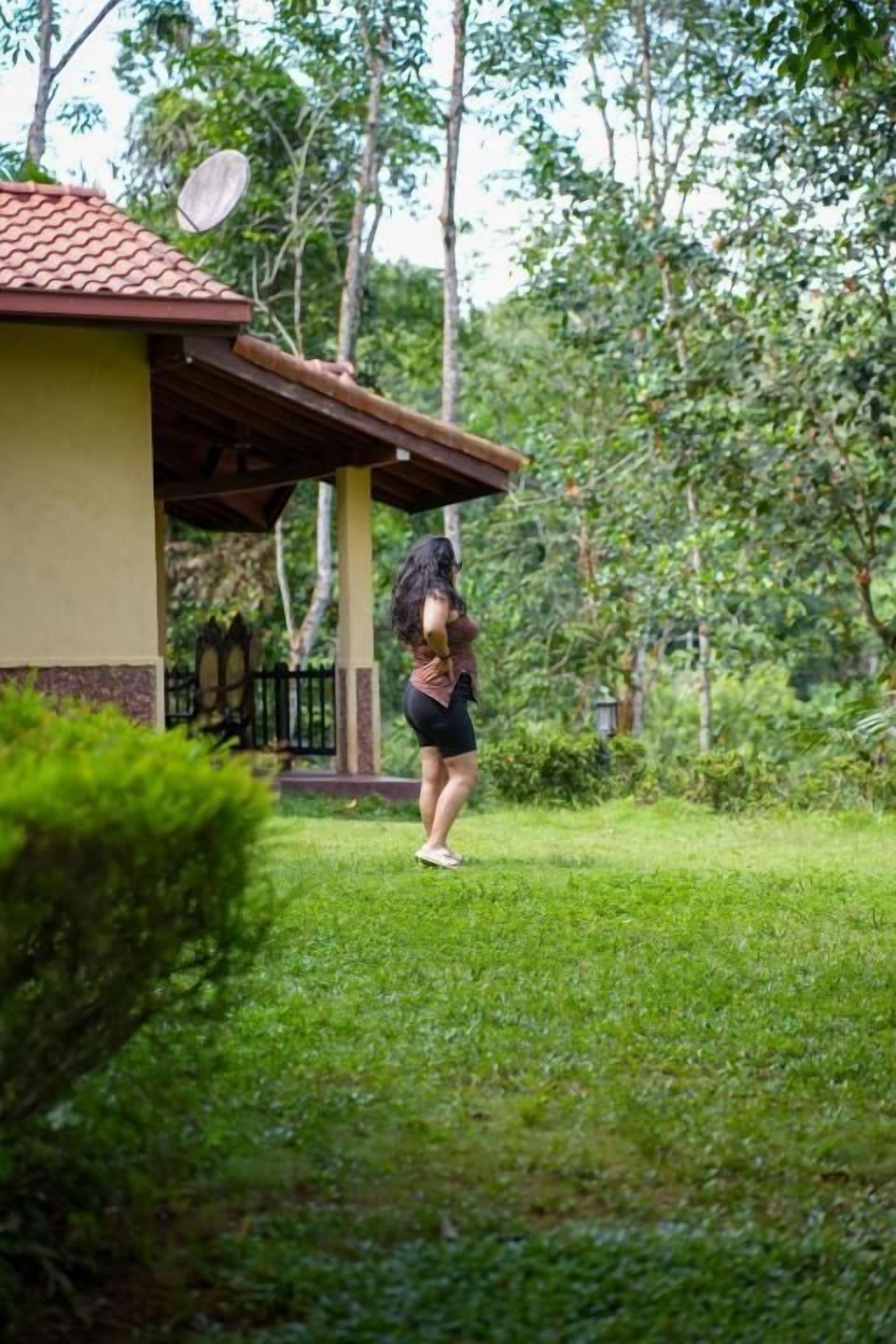 Una persona parada en un exuberante jardín verde, con un edificio al fondo.